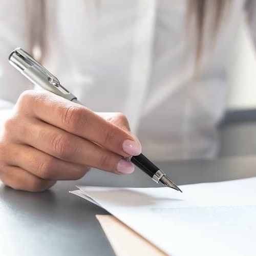 A woman about to sign some documents with a pen.
