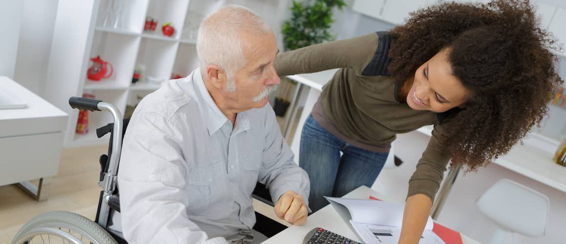 A young woman assisting an elderly man in a wheelchair, potentially related to refinancing or homeownership.