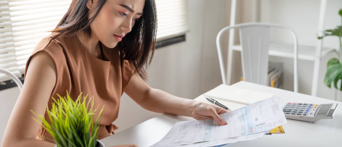 Confused young asian woman in a brown shirt looking at bills.