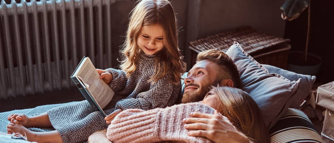 A couple enjoying with their daughter who is holding a book.