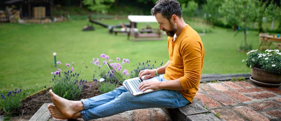 Man on laptop, barefoot, relaxing on porch in backyard.