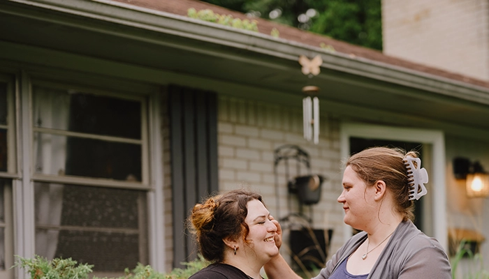Two people holding hands in front of small grey brick house.
