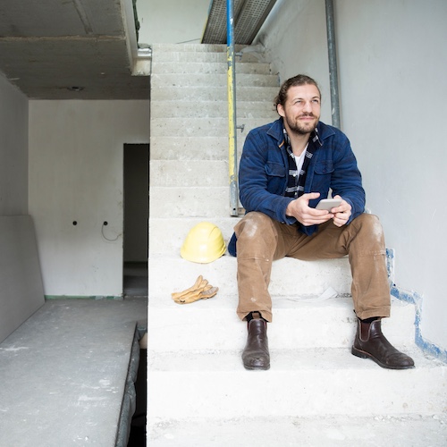 Construction worker sitting on staircase of home under renovation.