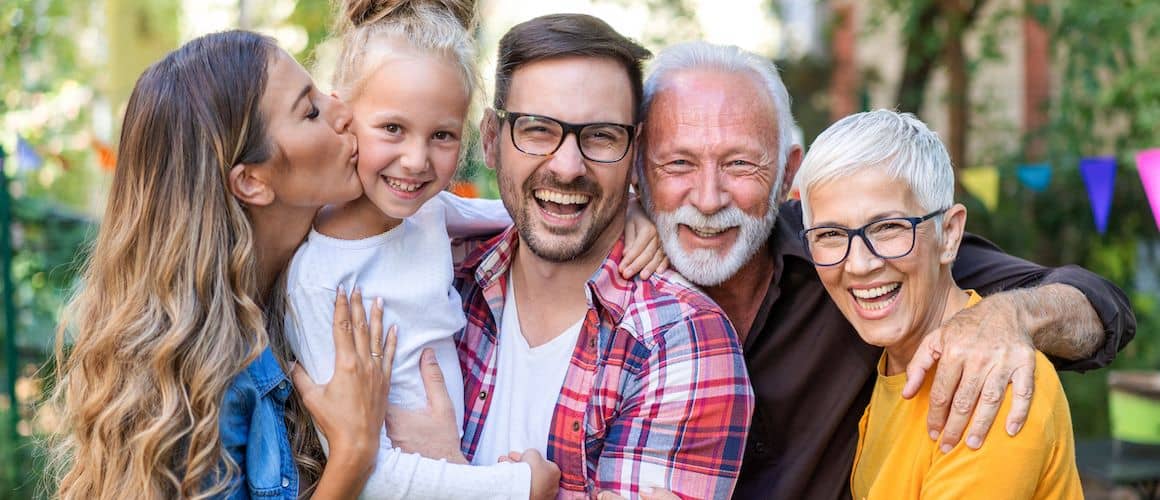 Multiple generations of a family smiling outdoors, portraying family bonding and unity across different age groups.