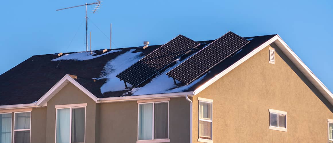 Two angled solar panels on a snowy house roof.