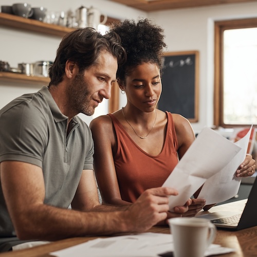 Couple looking at paperwork and looking pleased while sitting in a bright kitchen.