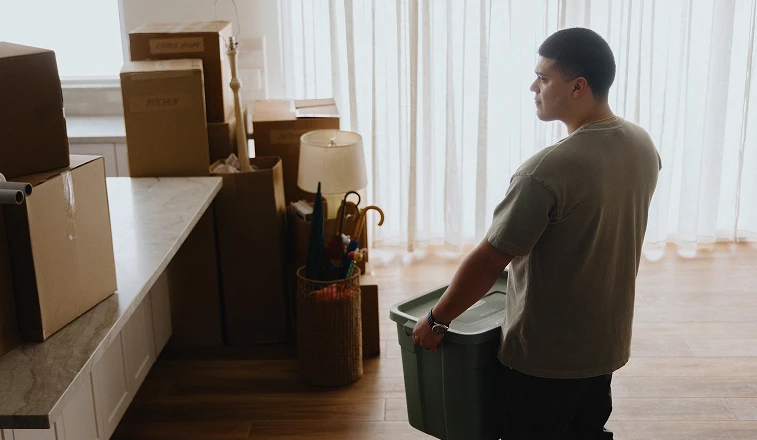 A man holding a box looks around his empty kitchen while moving into a new home.
