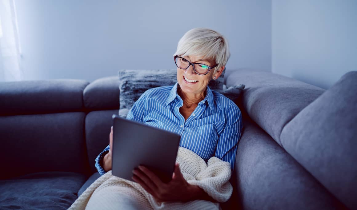 A woman using an iPad on a couch, representing modern living or technology use at home.