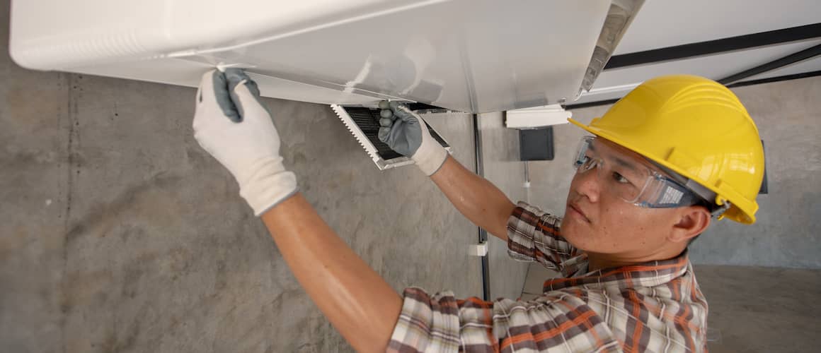 Man repairing HVAC wearing yellow hard hat.