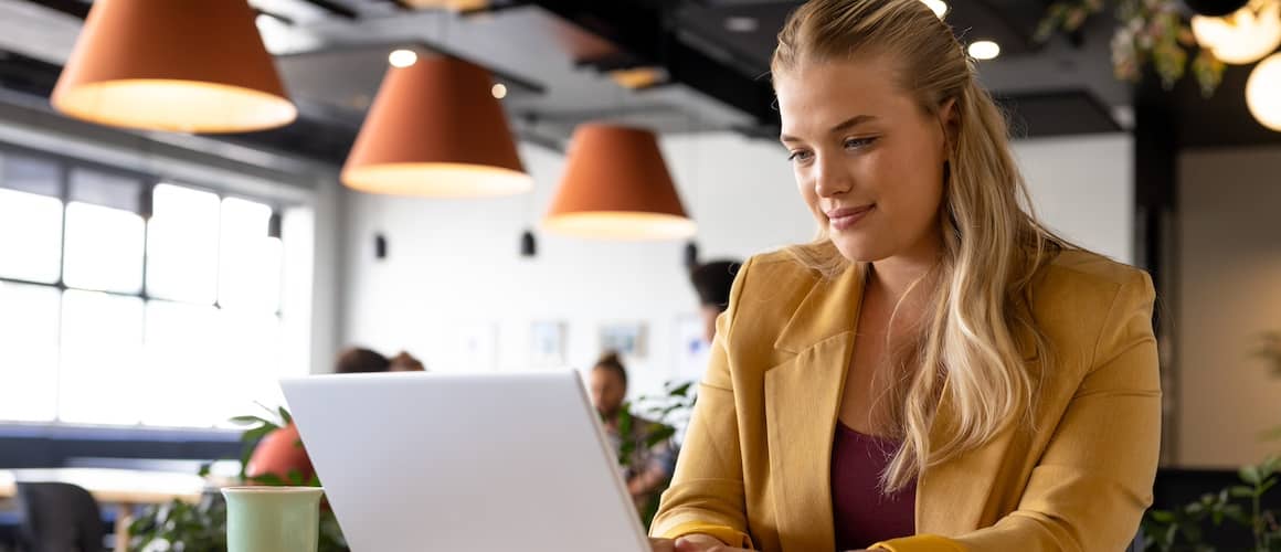 Woman sitting at open laptop at a cafe, smiling.
