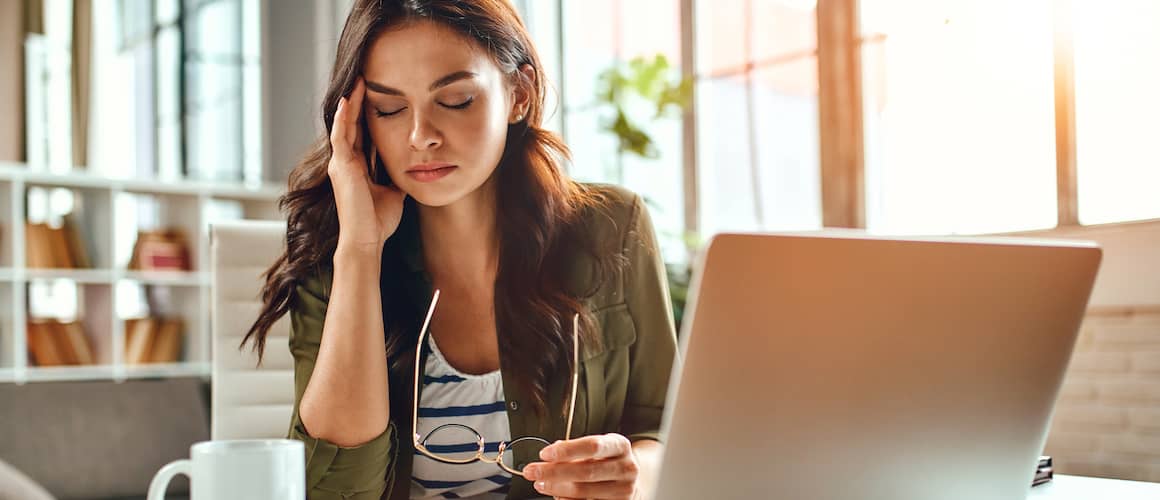 Young woman at home looking stressed in front of her laptop.