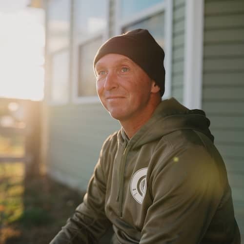 Man with hat smiling in setting sun.