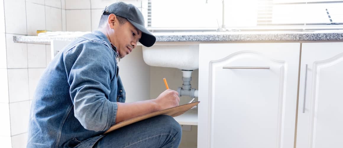 Home inspector with clip board checking underneath the sink.