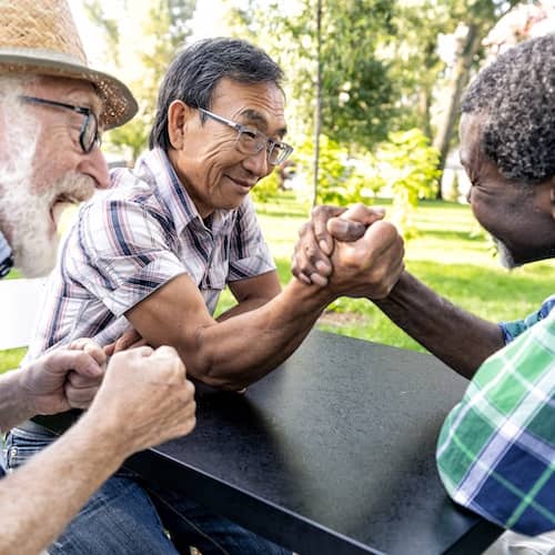 Two friends arm wrestle while a third cheers them on.