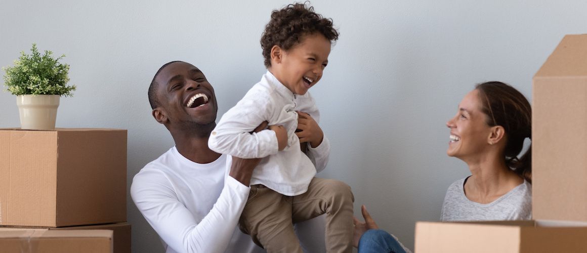 Young family moving into new home surrounded by boxes and smiling.