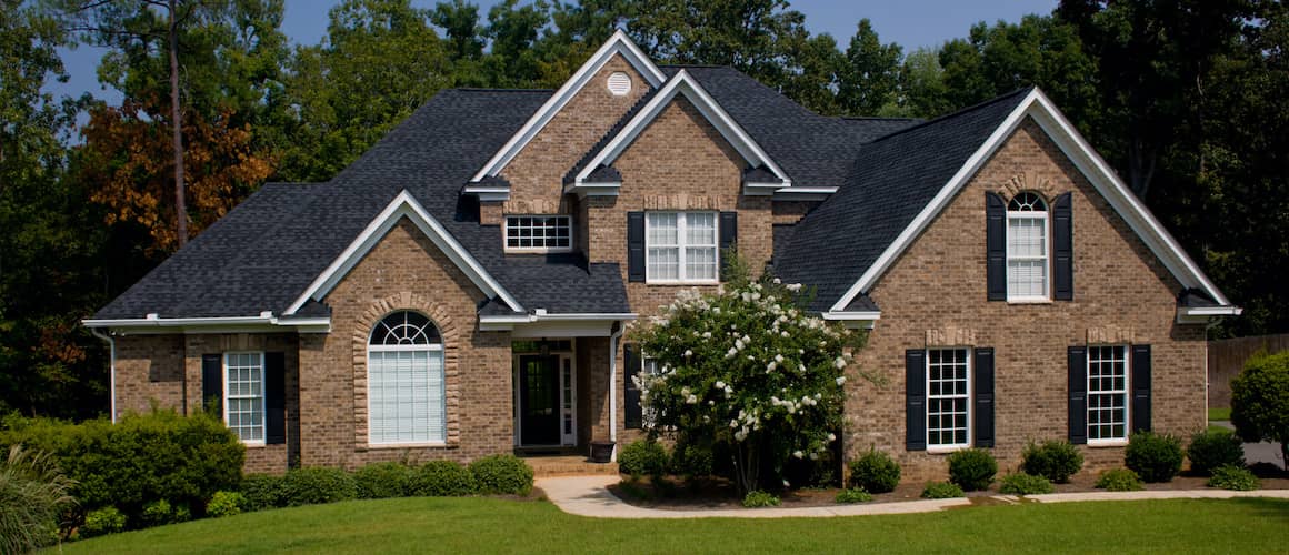 Brown brick house with a black roof and shutters, showcasing a specific architectural design of a residential property.