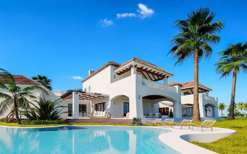 White house with Spanish tile roof, large pool, and palm trees.