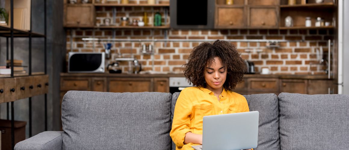 Woman working with a laptop on a couch, potentially managing finances or exploring real estate options online.