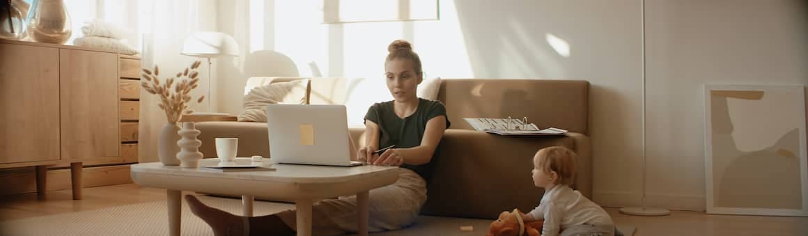 A women working from home on her laptop with her kid nearby.