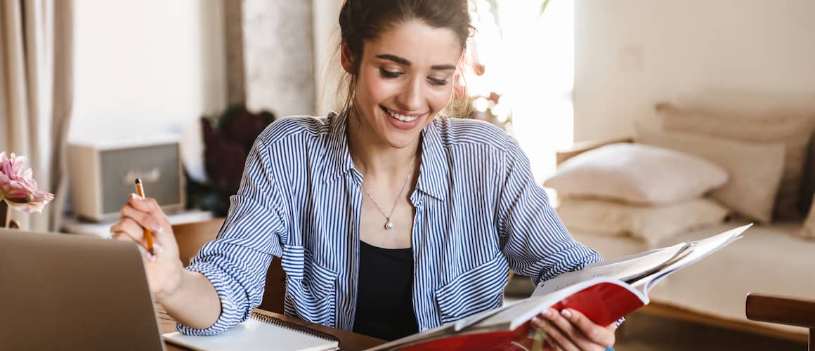 pretty woman studying with textbooks and using laptop at home