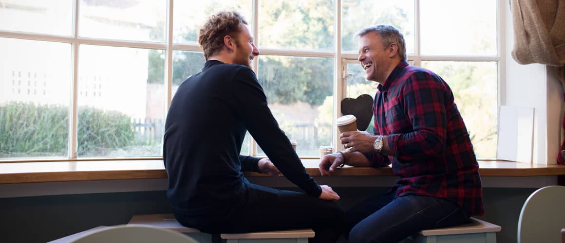 Men having coffee on a window seat chatting.