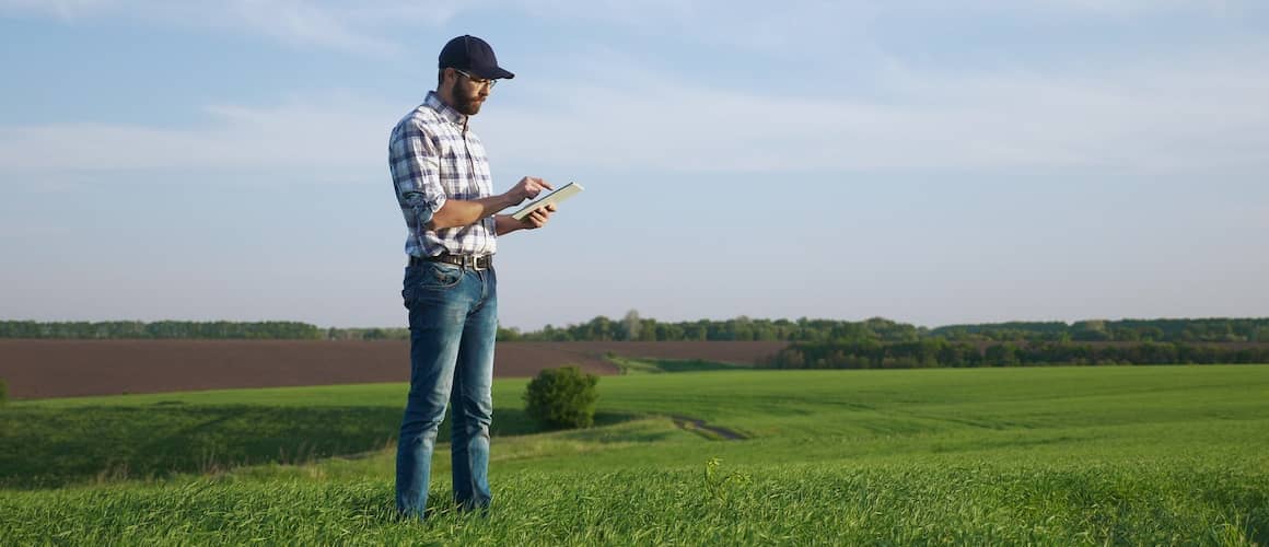 RHB Assets From IGX: Man holding a tablet and standing in an open field with a construction site in the background.