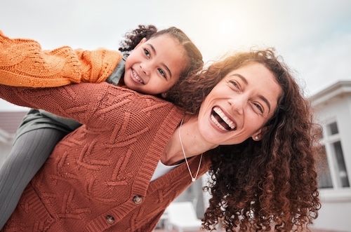 Smiling mother giving daughter a piggy back ride in yard of new home.