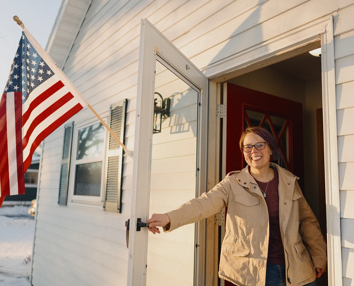 Person opening the front door of a home with an American flag