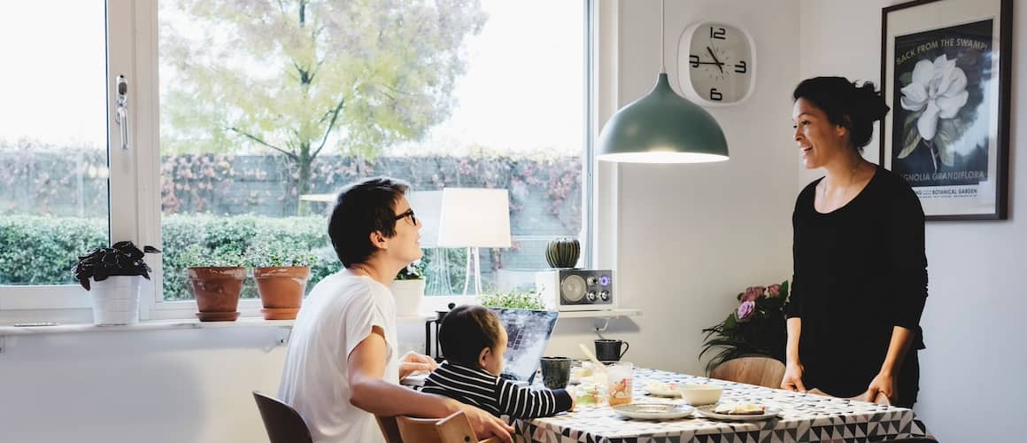 Moms chatting at kitchen table with young son eating nearby.