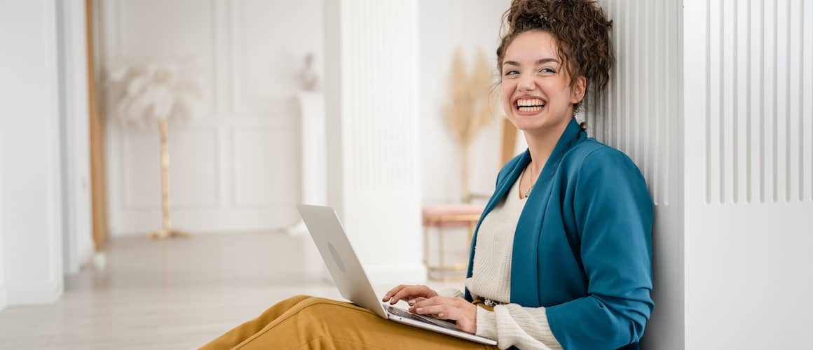 Young woman smiling, budgeting on her laptop in minimalist home.