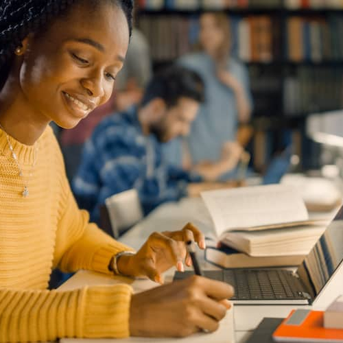 A black woman writing notes in a library or study setting.
