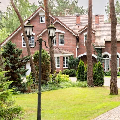 Cobbled driveway leading to a large brick home set back in the woods. 
