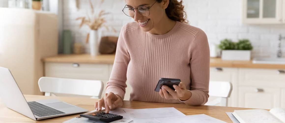 Woman working on computer with calculator.