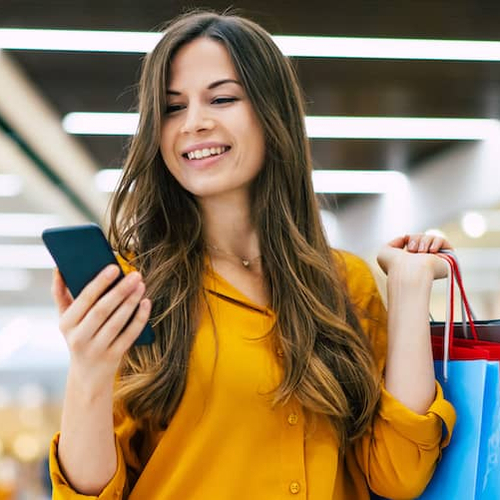 Young woman in yellow shirt checking her phone while shopping.