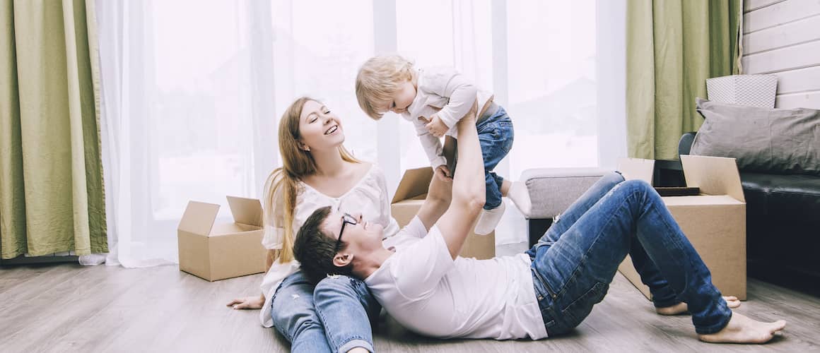 A young happy family with a little baby and boxes, likely in a new home, indicating a move or relocation.