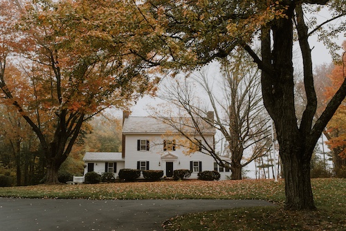 White two story home with large grassy yard and big trees in autumn.