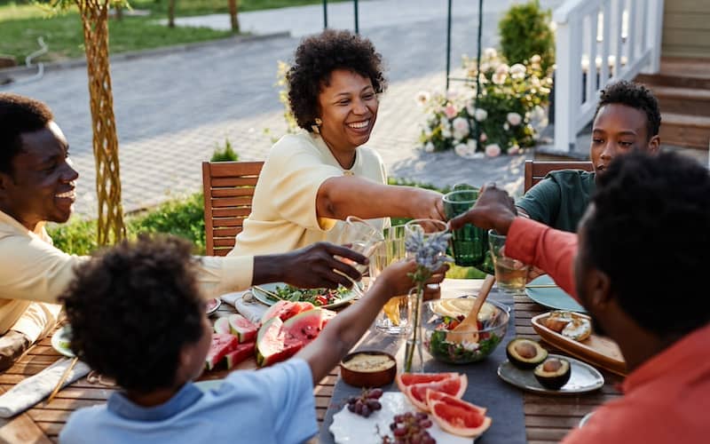 Family sitting at the table outside cheers-ing with summer drinks and smiling.