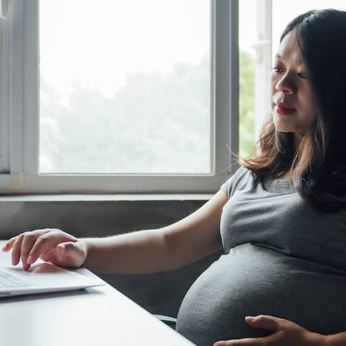 A pregnant Asian woman browsing or working on a computer, possibly researching or organizing information online.