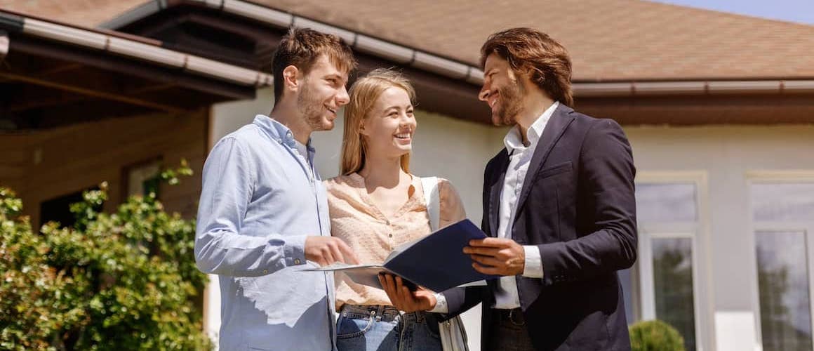 Real estate agent with young couple on front lawn of house.