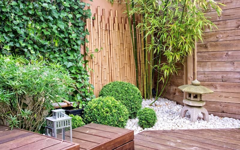 Zen themed garden with bright green foliage, bamboo and wood slat walls and ornamentation on white stone. 