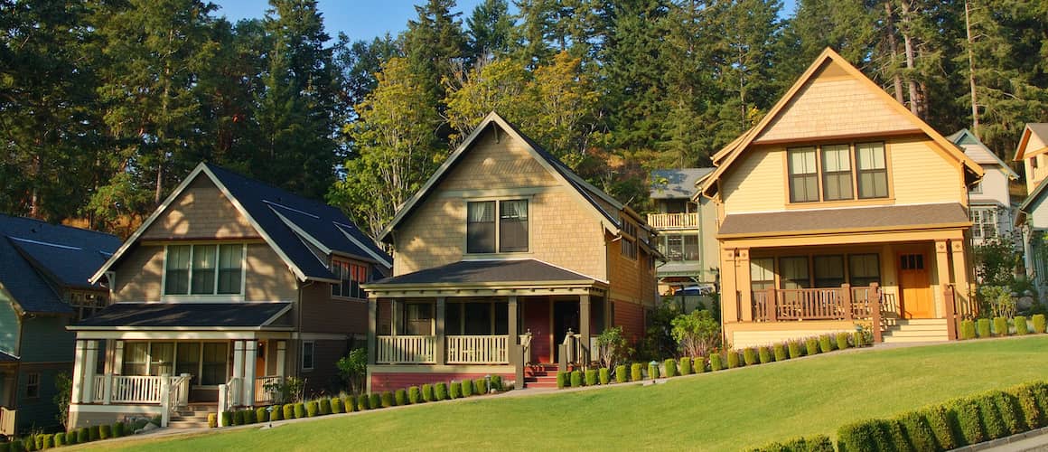 A series of three houses on a hill with an evergreen forest behind them.