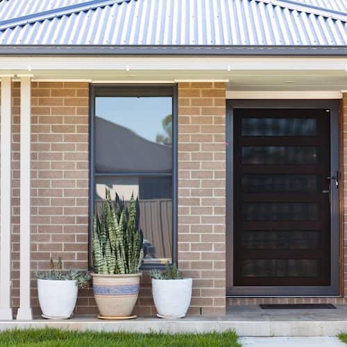 Front entrance of brick ranch home with black door and potted plants.