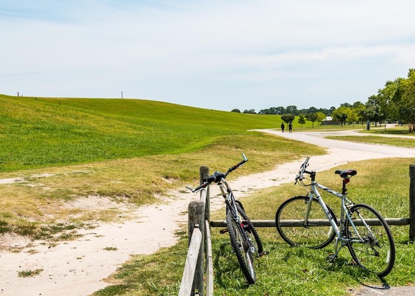 Two bicycles rest on a fence while people trail hike at Mount Trashmore Park.