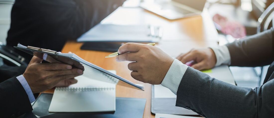 Businessmen looking at and discussing something on a clipboard at a meeting.