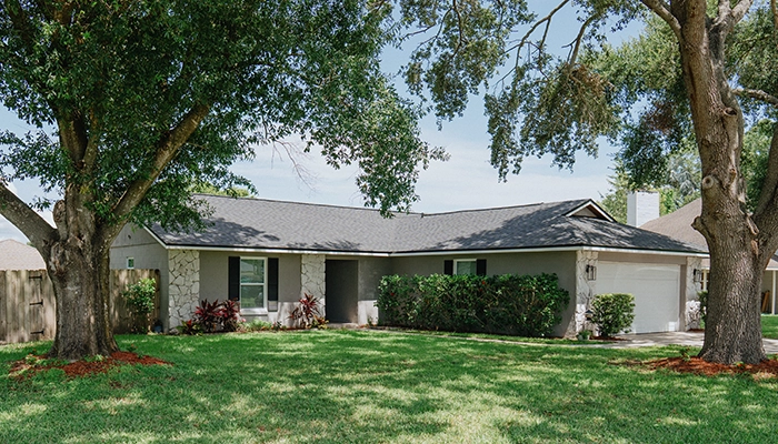 Ranch-style home with stone features and two large trees out front.