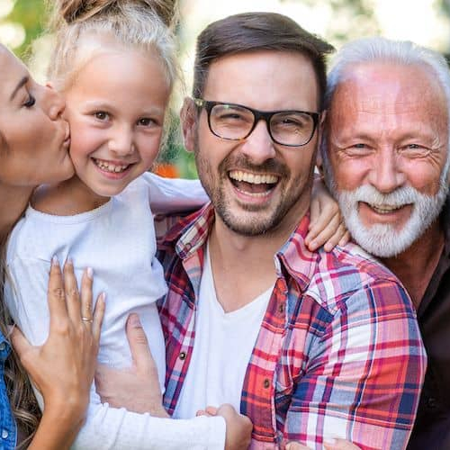 Multiple generations of a family smiling outdoors, portraying family bonding and unity across different age groups.