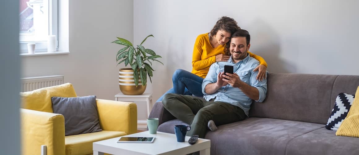 Couple on couch snuggled together and smiling while looking at phone together.