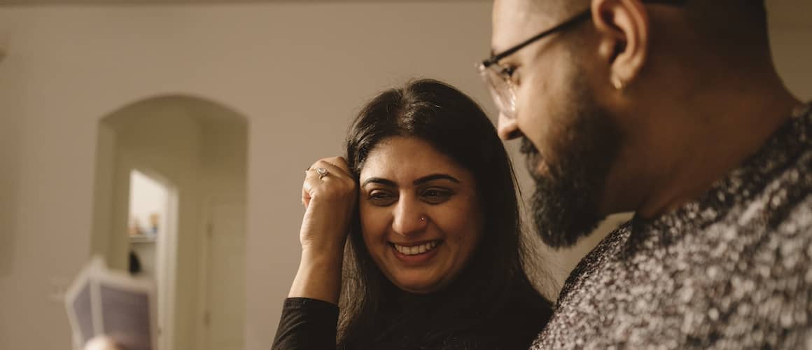 Couple sitting on couch and smiling at one another.