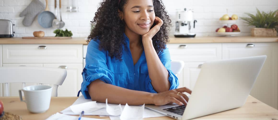 An Afro-American woman using a portable computer and smiling, potentially in a home setting.