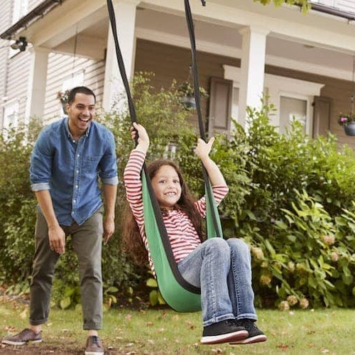 A father swinging his daughter in front yard of a house.